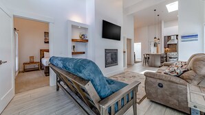 A modern living room with a sofa, a bench, a flat-screen TV, and a kitchen area in the background.