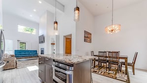 A modern kitchen with a central island, stainless steel appliances, pendant lighting, and a dining area with a wooden table and chairs.