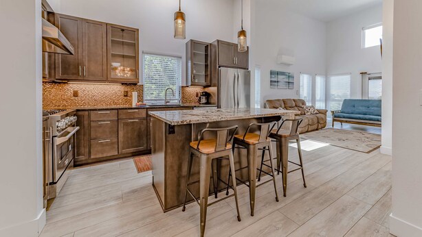 A modern kitchen with a large island, bar stools, and a dining area with a sofa and coffee table.