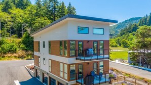 A multi-story building with balconies, large windows, and a view of a forested hillside.