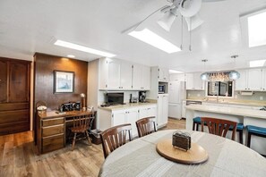Une cuisine moderne avec des meubles blancs, un coin repas doté d’une table ronde et un ventilateur de plafond.