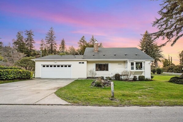 Une maison de plain-pied avec un garage, une cheminée et un jardin devant.