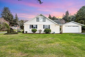Une maison de plain-pied avec un garage, entourée d’une pelouse bien entretenue et d’arbres.
