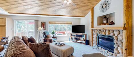 A spacious living room with a stone fireplace, wooden ceiling, and a television.