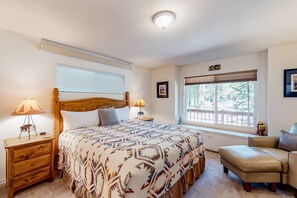 Un dormitorio con una cama, dos mesitas de noche con lámparas, una silla, un ventanal con persianas y una puerta con un letrero.