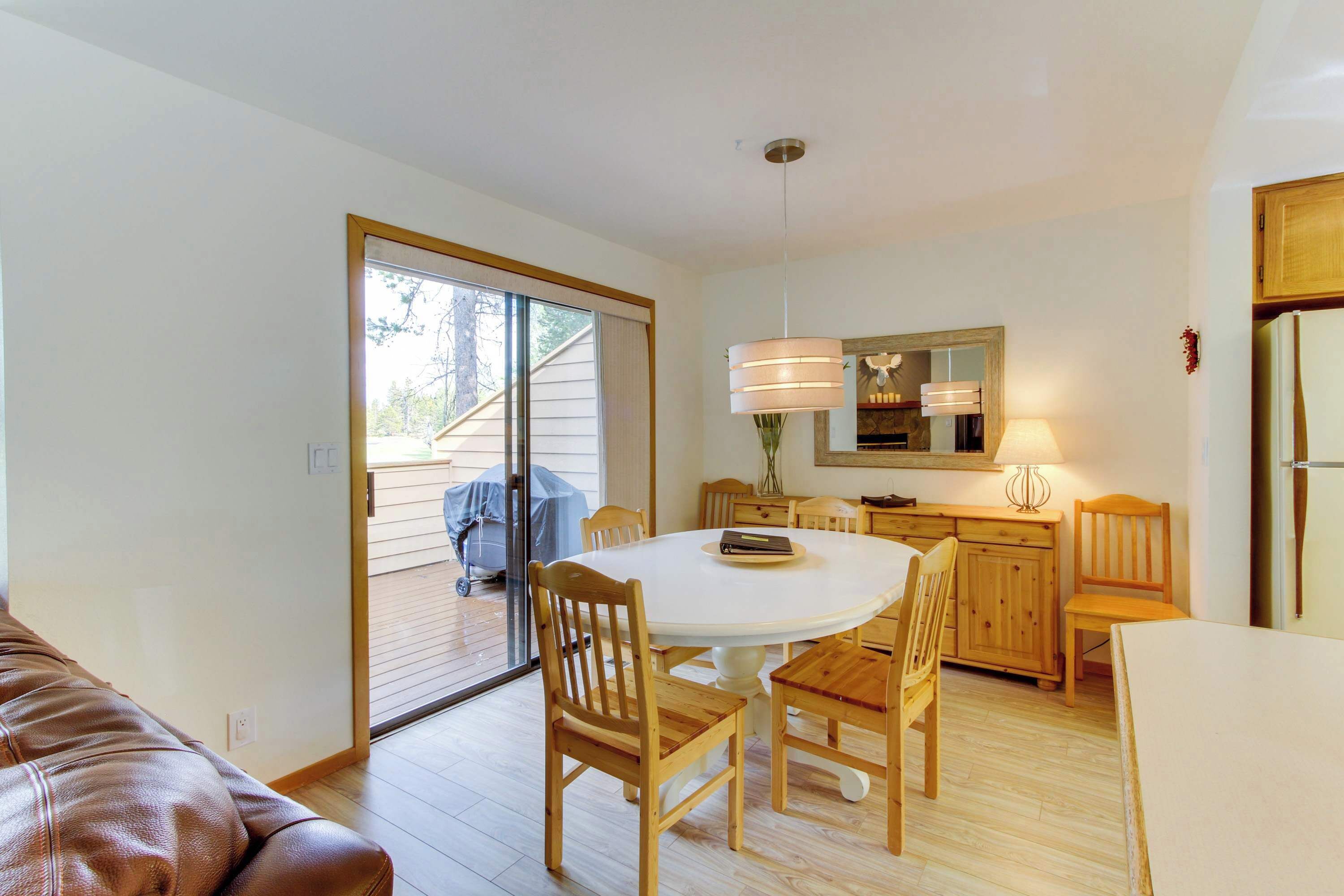 A dining area with a round table, wooden chairs, a kitchen with a refrigerator, and a sliding glass door leading to an outdoor area.