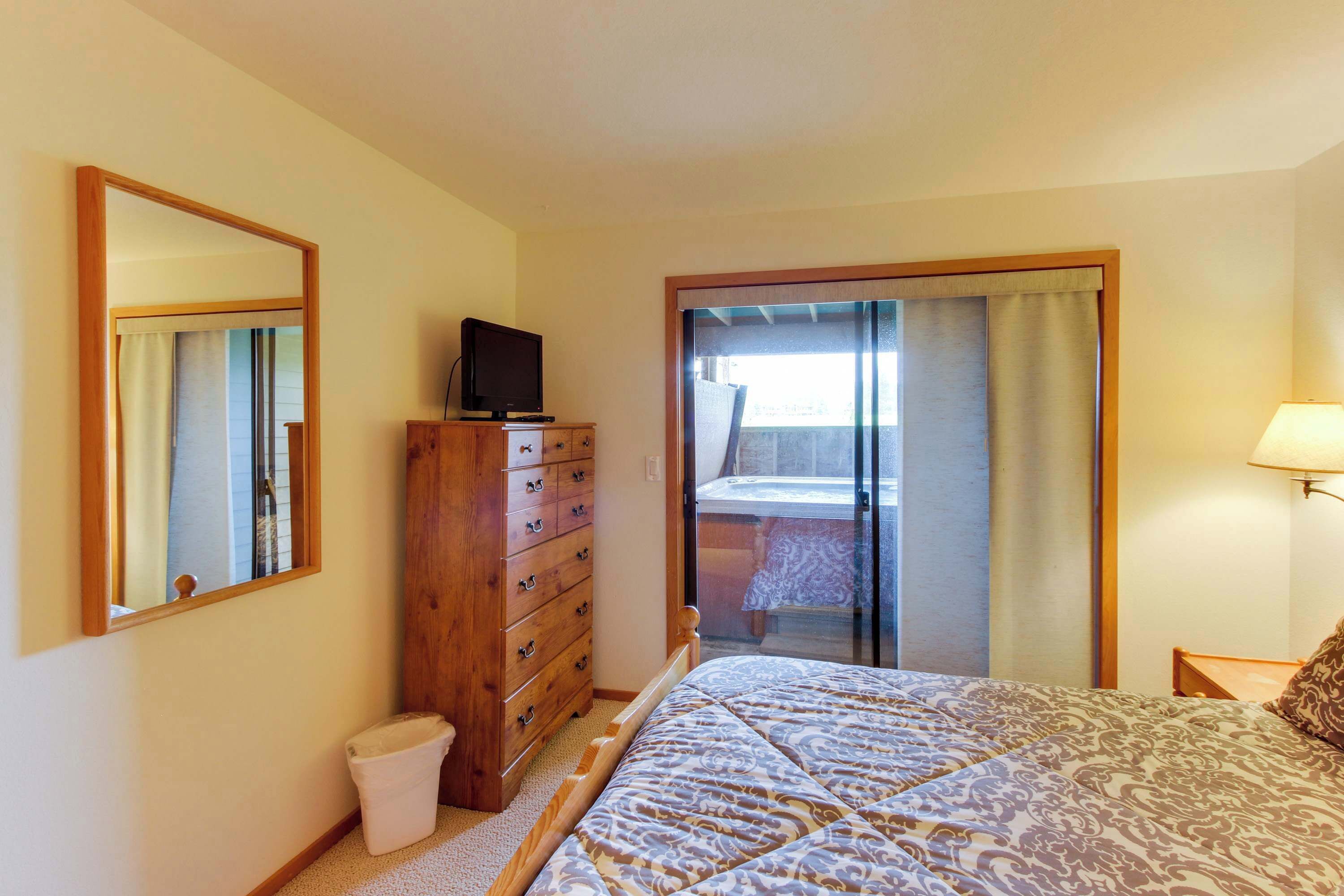 A bedroom with a bed, a wooden dresser, a television, a window with curtains, and a lamp.