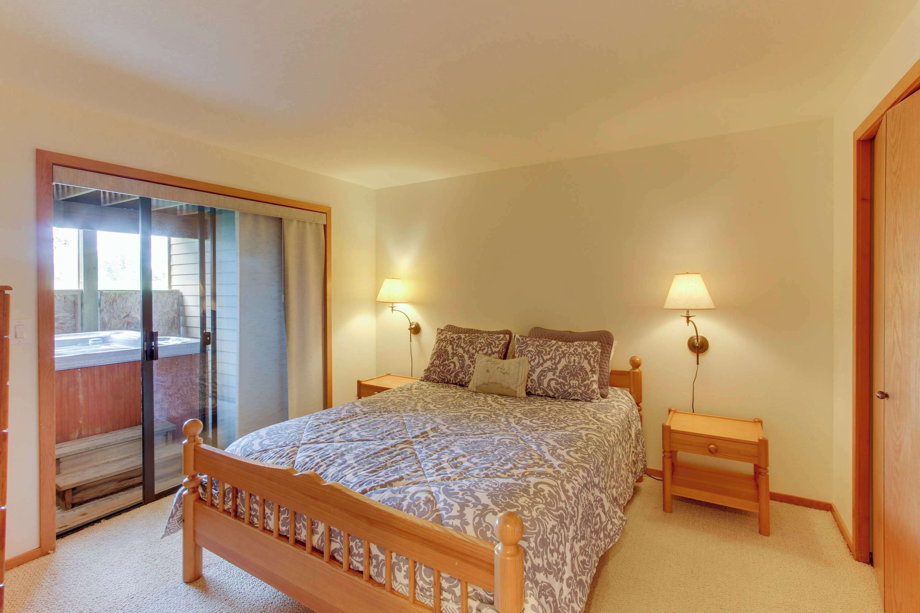 A bedroom with a bed, two bedside lamps, a wooden nightstand, a sliding glass door leading to a balcony, and a wooden door.