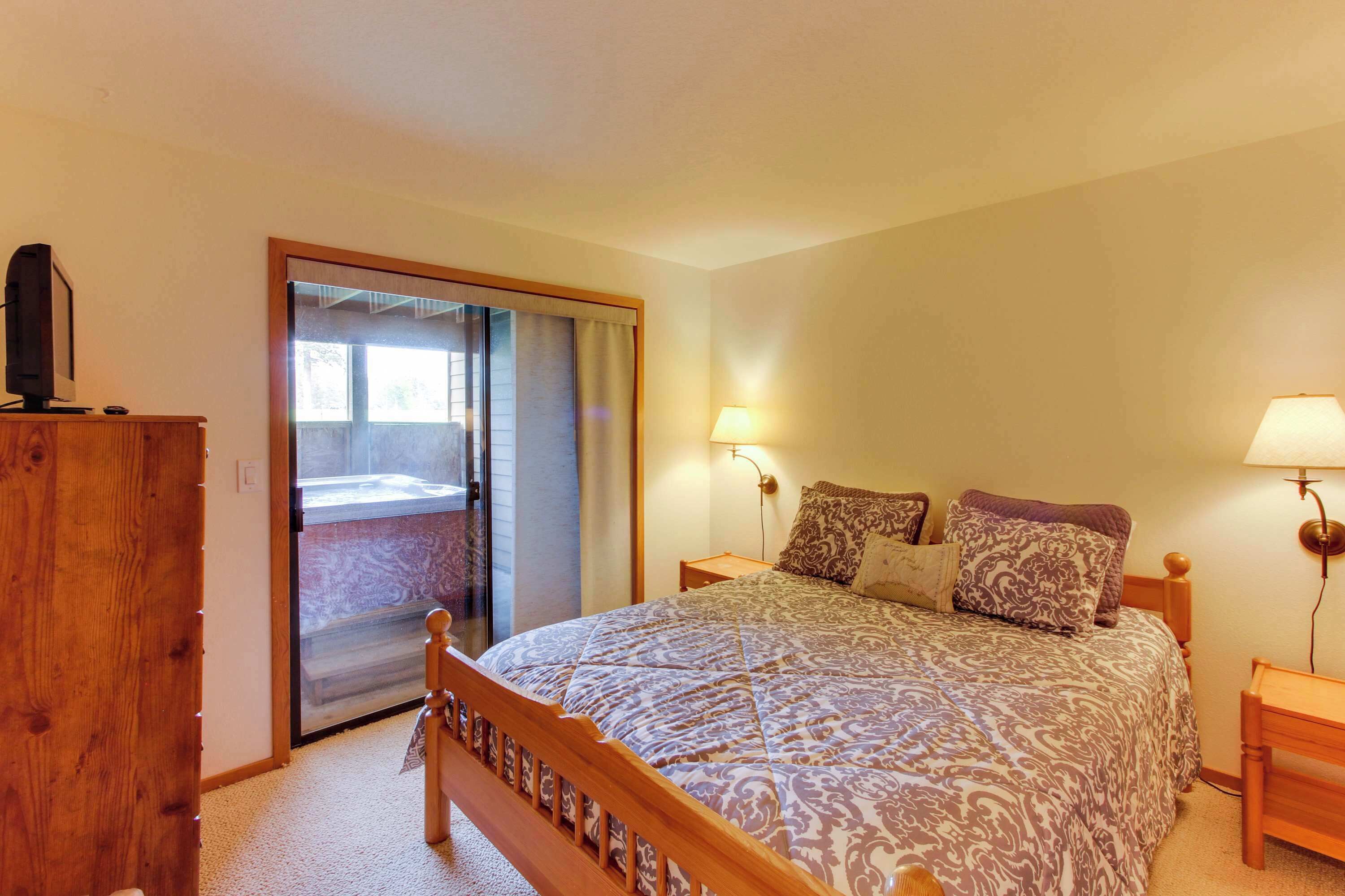A bedroom with a bed, a wooden wardrobe, a desk, two bedside lamps, and a sliding glass door leading to a balcony.