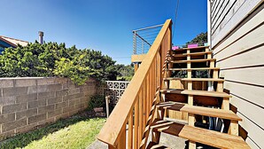 A wooden staircase leading to a deck, surrounded by a brick wall and greenery.