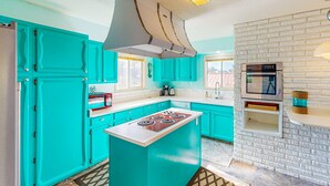 A kitchen with teal cabinets, a central island with a stove, a microwave, and a built-in oven.