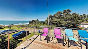 A wooden deck with outdoor seating, a view of the ocean, and parked cars.