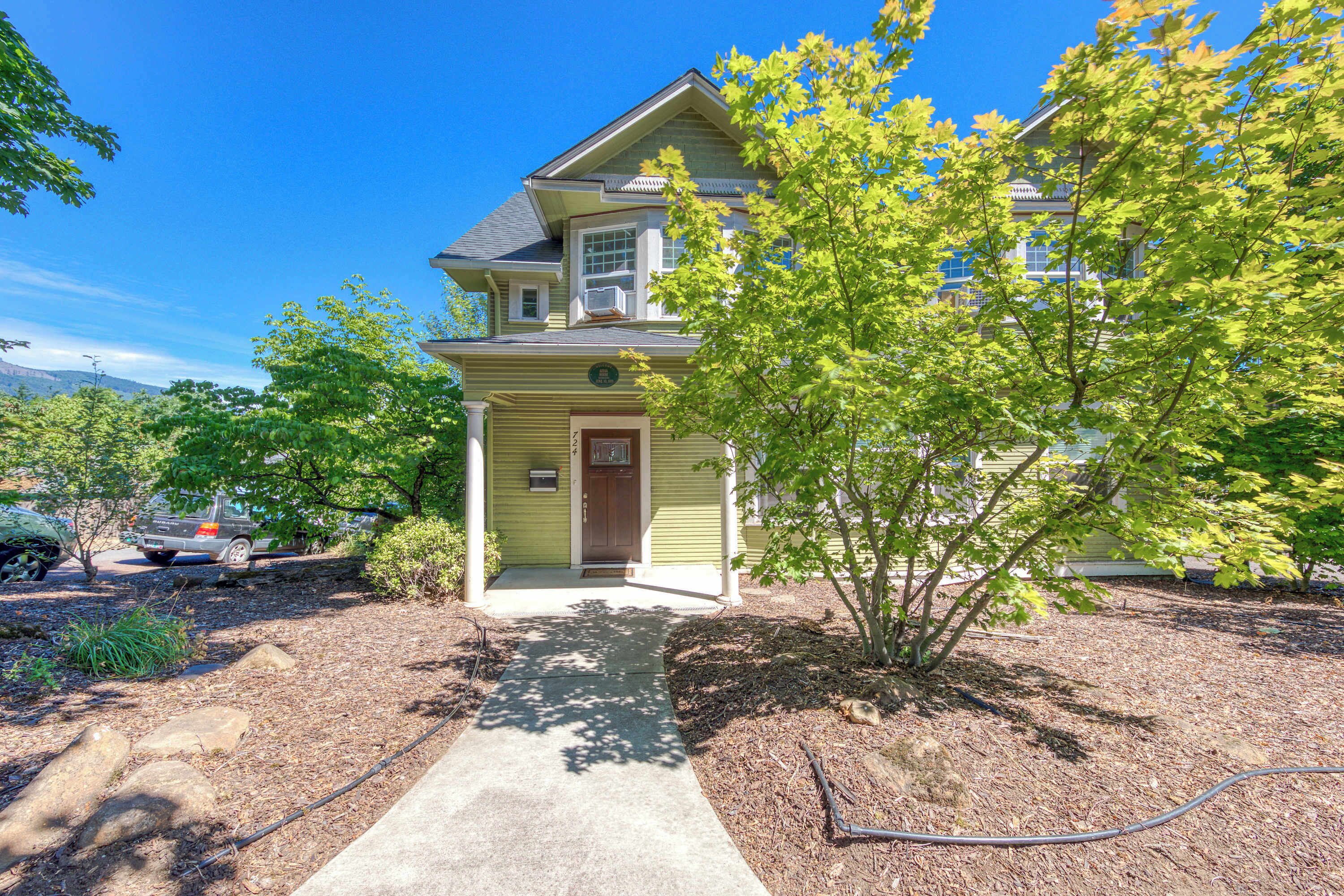 A two-story house with a front porch, a driveway, and a tree in the yard.