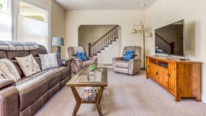 Un salon avec un canapé en cuir marron, deux fauteuils, une table basse, un meuble en bois, un téléviseur et un escalier.
