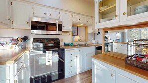 Cocina con armarios blancos, electrodomésticos de acero inoxidable y encimera de madera.