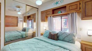 Un dormitorio con cama, espejo, armarios de madera, ventilador de techo y ventana con cortinas.