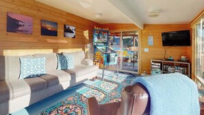 Un acogedor interior de cabaña con un sofá, televisión, estantería y una alfombra colorida.