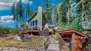 Une cabane avec un sentier de pierres menant à une terrasse en bois, entourée de grands arbres.