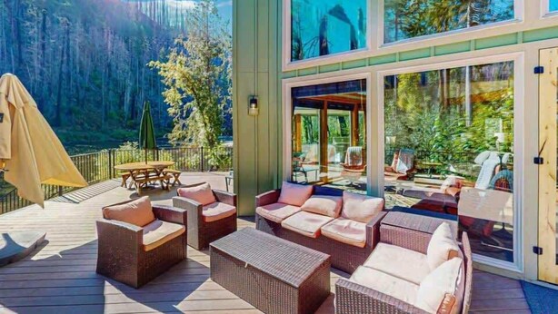 Une terrasse dotée de meubles en osier, de portes vitrées et offrant une vue sur une montagne boisée.
