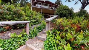 A multi-level building with a wooden deck and a stone staircase surrounded by lush greenery. - 2-story dog-friendly, private hot tub, deck, gas grill, wood stove, ocean view, level 2 EV charger (Manzanita)