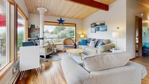 A modern living room with a wooden ceiling, a star decoration, a sofa, a coffee table, and a wicker chair. - 2-story dog-friendly, private hot tub, deck, gas grill, wood stove, ocean view, level 2 EV charger (Manzanita)