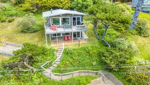 A two-story house with a balcony, surrounded by lush greenery and a paved pathway. - 2-story dog-friendly, private hot tub, deck, gas grill, wood stove, ocean view, level 2 EV charger (Manzanita)