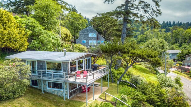 A modern house with a balcony, surrounded by lush greenery and trees. - 2-story dog-friendly, private hot tub, deck, gas grill, wood stove, ocean view, level 2 EV charger (Manzanita)