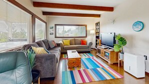A living room with a sofa, a coffee table, a TV, a bookshelf, and a radiator. - 2-story dog-friendly, private hot tub, deck, gas grill, wood stove, ocean view, level 2 EV charger (Manzanita)
