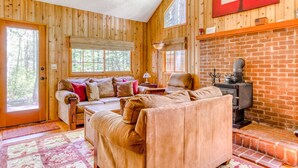 A wooden cabin interior with a sofa, fireplace, and large windows. - Modern, cozy, dog-friendly mountain retreat in central location (Rhododendron)