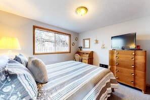 Une chambre à coucher avec un lit, une commode, une télévision, une fenêtre et une lampe.
