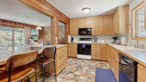 A kitchen with wooden cabinets, a microwave, stove, and a dining area with chairs and a table. - Spacious home with full kitchen, wifi, private backyard & grill (Welches)