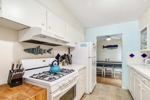 Una cocina con armarios blancos, estufa, refrigerador y un comedor con sillas.