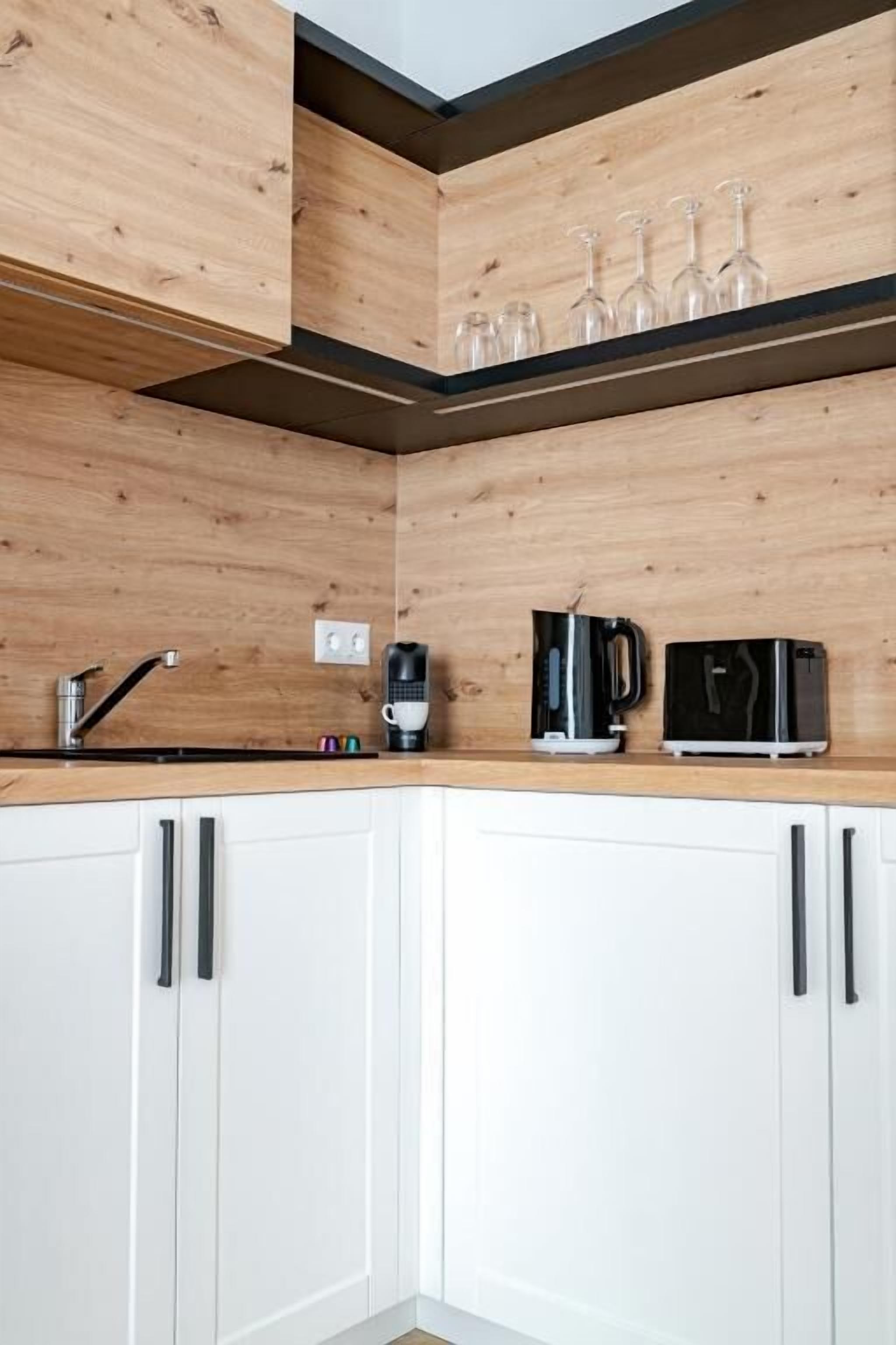 Una cocina con armarios de madera, cafetera, tostadora y copas de vino en un estante.