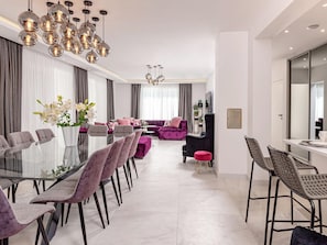 A modern living room with a glass dining table, purple sofas, and a chandelier. - 5-bedroom Estate With Heated Pool (Kastela)