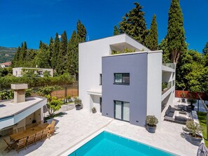 A modern two-story house with a swimming pool, outdoor seating, and a view of the surrounding forest. - 5-bedroom Estate With Heated Pool (Kastela)