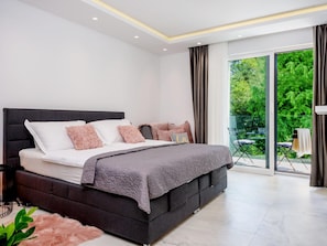 A modern bedroom with a large bed, a balcony with a view of greenery, and a sliding glass door. - 5-bedroom Estate With Heated Pool (Kastela)