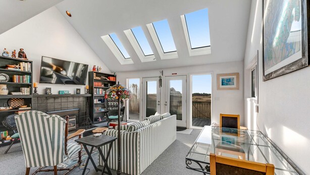 A modern living room with a fireplace, striped furniture, a glass table, and skylights. - Family-Friendly, Waterfront Home with Free WiFi, Gas Fireplace, & Private W/D (Long Beach)