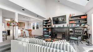 A modern living room with striped sofas, a fireplace, bookshelves, and a large TV. - Family-Friendly, Waterfront Home with Free WiFi, Gas Fireplace, & Private W/D (Long Beach)