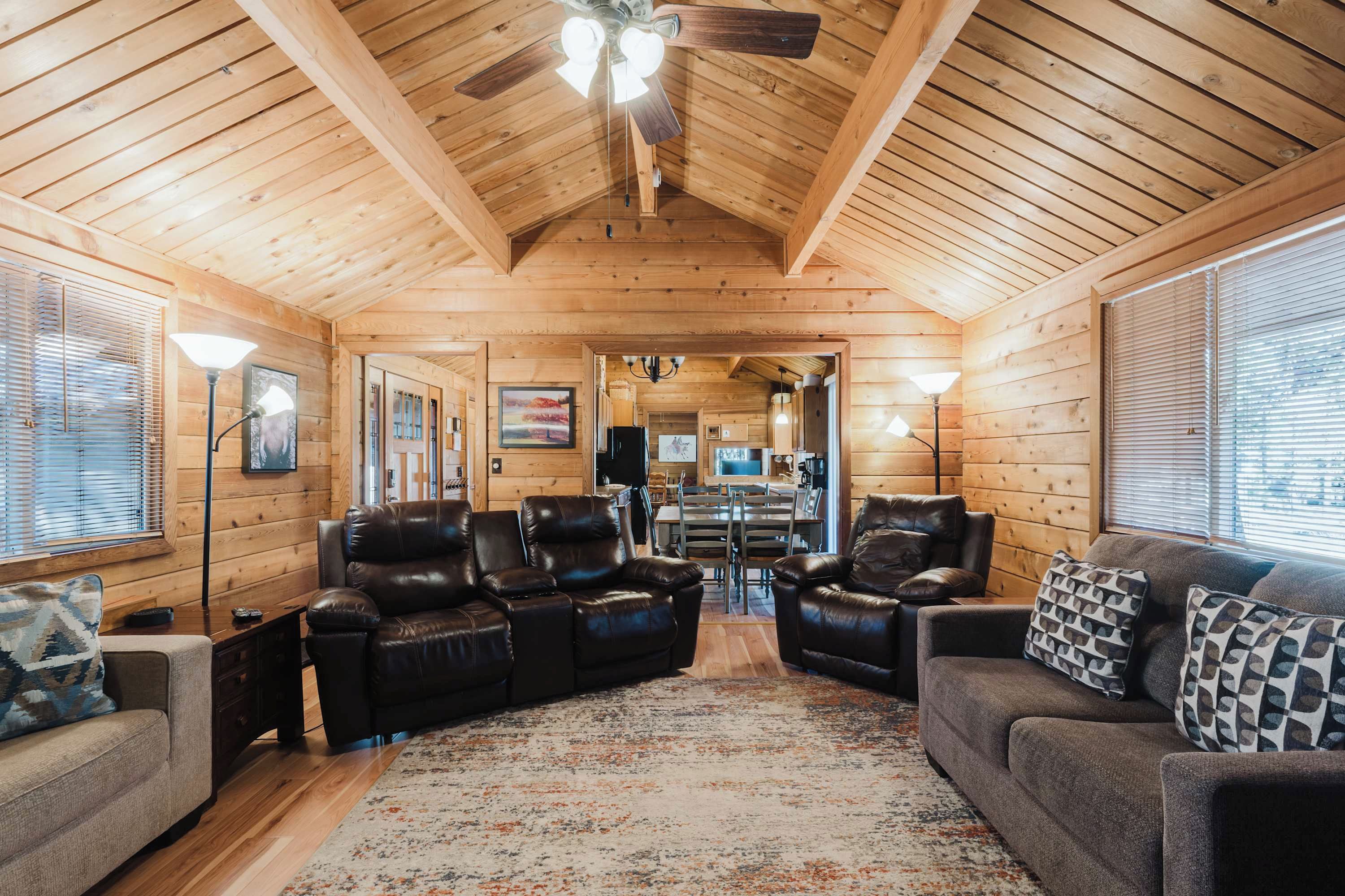 A log cabin interior with leather sofas, a dining area, and a ceiling fan.