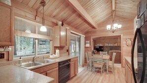 Interior de una cabaña de madera con cocina que incluye lavavajillas, doble pileta y comedor con sillas.