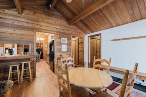 A wooden interior with a dining area, kitchen, and a view of the outside. - Woodsy Cabin with Private Hot Tub, Game Tables & 8 SHARC Passes - Dogs OK (Sunriver)