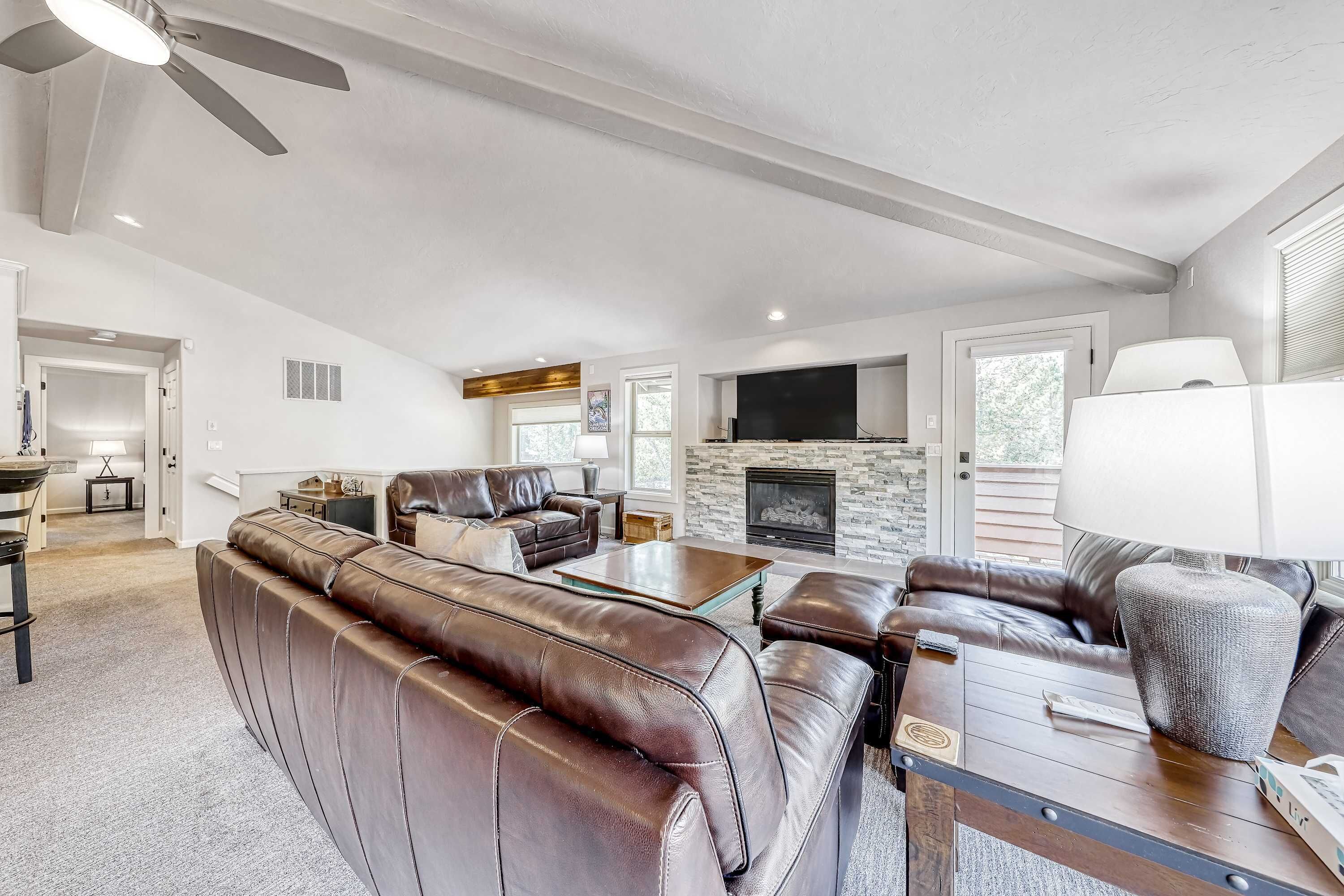 A spacious living room with leather sofas, a fireplace, a television, and a ceiling fan.