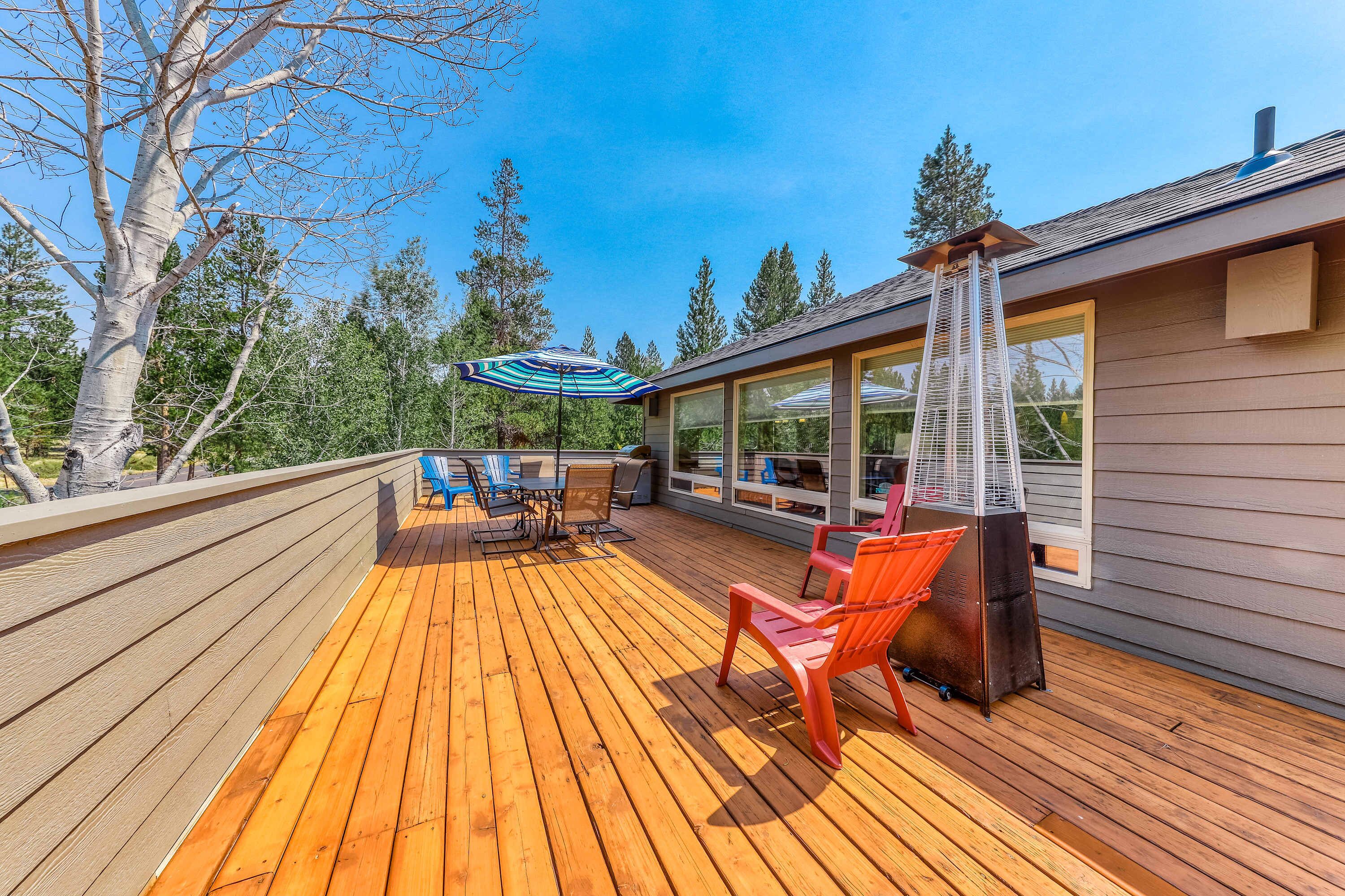 A wooden deck with outdoor furniture, a grill, and a large window overlooking a forest.