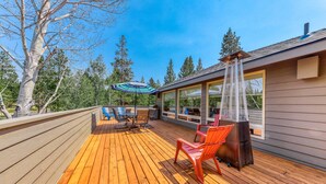 Eine Holzterrasse mit Gartenmöbeln, einem Grill und einem großen Fenster mit Blick auf einen Wald.
