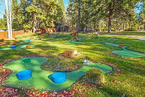 A miniature golf course with multiple holes, trees, and a clear sky.