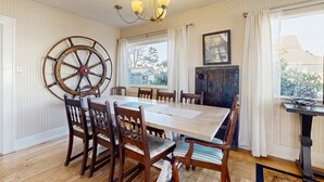 Een eetkamer met een houten tafel, stoelen, een decoratie van een scheepsschroef, een kroonluchter en uitzicht door het raam.