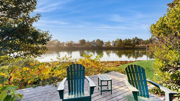 Een terras met twee Adirondack-stoelen gericht op een rustig meer, omgeven door bomen en begroeiing.