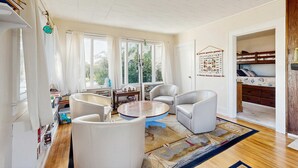 Een kamer met een ronde houten tafel, witte lederen stoelen, een boekenplank en een stapelbed op de achtergrond.