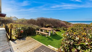 A wooden deck leading to a grassy area with a picnic table and benches, overlooking a coastal landscape.