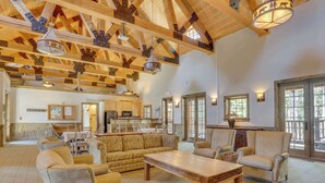 A spacious living area with a high ceiling, wooden beams, and a large window. - Riverfront mountain townhouse with pool & hot tub, patio, & easy ski access (Government Camp)